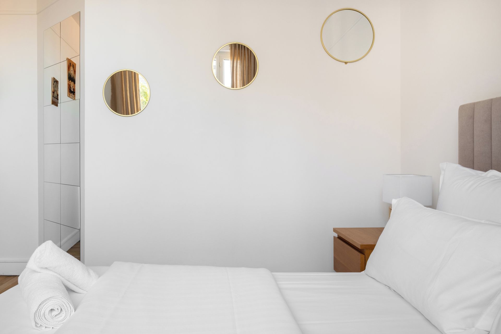 A hotel room with a bed, a wooden nightstand, a mirror, and a wall-mounted mirror.