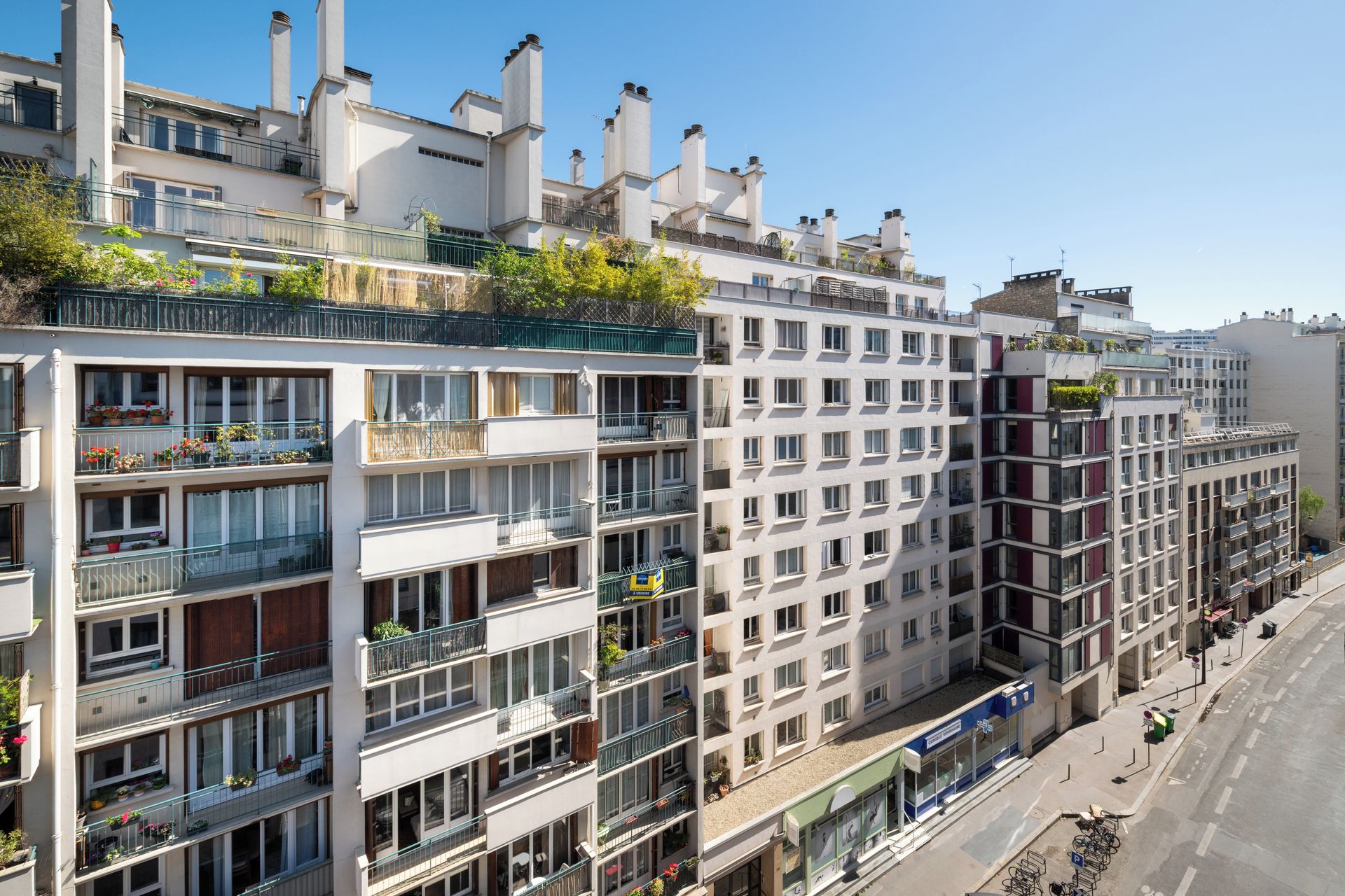 A multi-story residential building with balconies, a street view, and a clear sky.