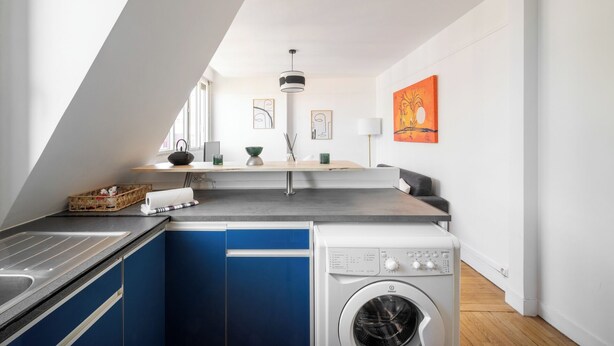 Een compacte keuken met een ingebouwde wasmachine, een zithoek met tafel en stoelen, en een raam voor natuurlijk licht.