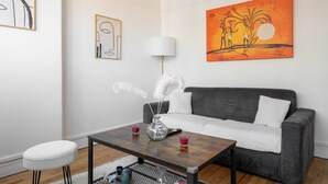 Een moderne woonkamer met een grijze bank, een houten salontafel, een witte ronde poef en een vloerlamp.