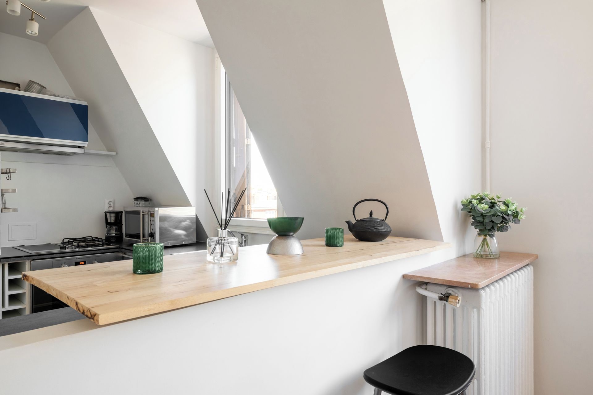 A modern kitchen with a sloped ceiling, a wooden countertop, and a black chair.