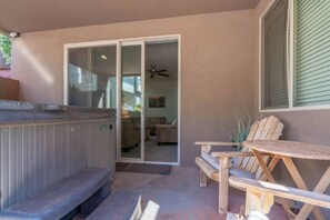 Ein Patio mit Whirlpool, Holzstühlen und einer Glastür zum Innenbereich.