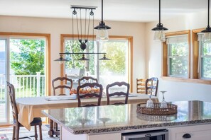 A kitchen with a granite countertop, wooden chairs, hanging pendant lights, and large windows. - Island View Escape: Lake, Private Beach, Deck, Firepit, Family, Game Room, more! (Broadalbin)
