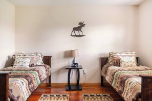 Ein Zimmer mit zwei Betten, einem kleinen Tisch mit Lampe und einer Wanddekoration – einem Elch.