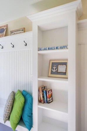 Ein weißes Zimmer mit einem an der Wand befestigten Kleiderhaken, einem Bücherregal und einem Schild mit der Aufschrift 'THE LAKE MAKES ME HAPPY'.