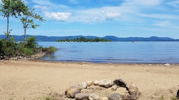 Une scène au bord du lac, avec un ciel dégagé, une plage de sable et un cercle de rochers au premier plan.