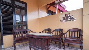 A patio with a round wooden table and four chairs, a window with blinds, and a decorative wall piece. - Koolkost Syariah Jalan Cangkringan Kaliurang (Ngemplak)
