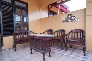 Un patio con una mesa redonda de madera y cuatro sillas, una ventana con persianas y un adorno en la pared.