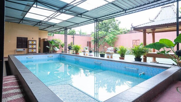 A swimming pool with a tiled edge, a covered roof, and potted plants around the pool area. - Koolkost Syariah Jalan Cangkringan Kaliurang (Ngemplak)