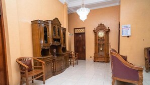 A room with a wooden cabinet, two chairs, a purple sofa, a wooden clock, and a chandelier. - Koolkost Syariah Jalan Cangkringan Kaliurang (Ngemplak)