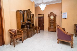Una habitación con un armario de madera, dos sillas, un sofá púrpura, un reloj de madera y una araña.