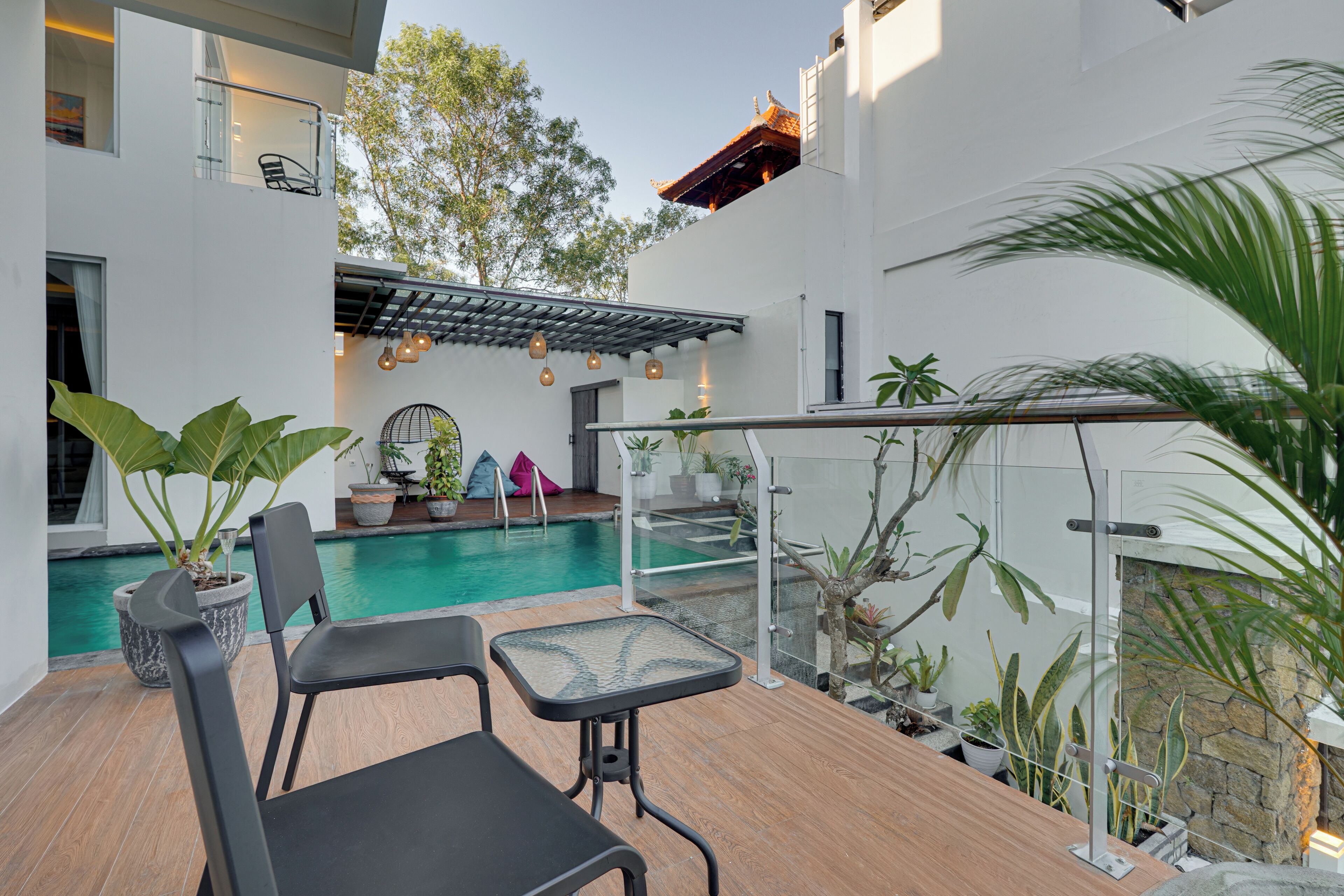Un área de piscina moderna al aire libre con barandilla de cristal, mobiliario y plantas en macetas.