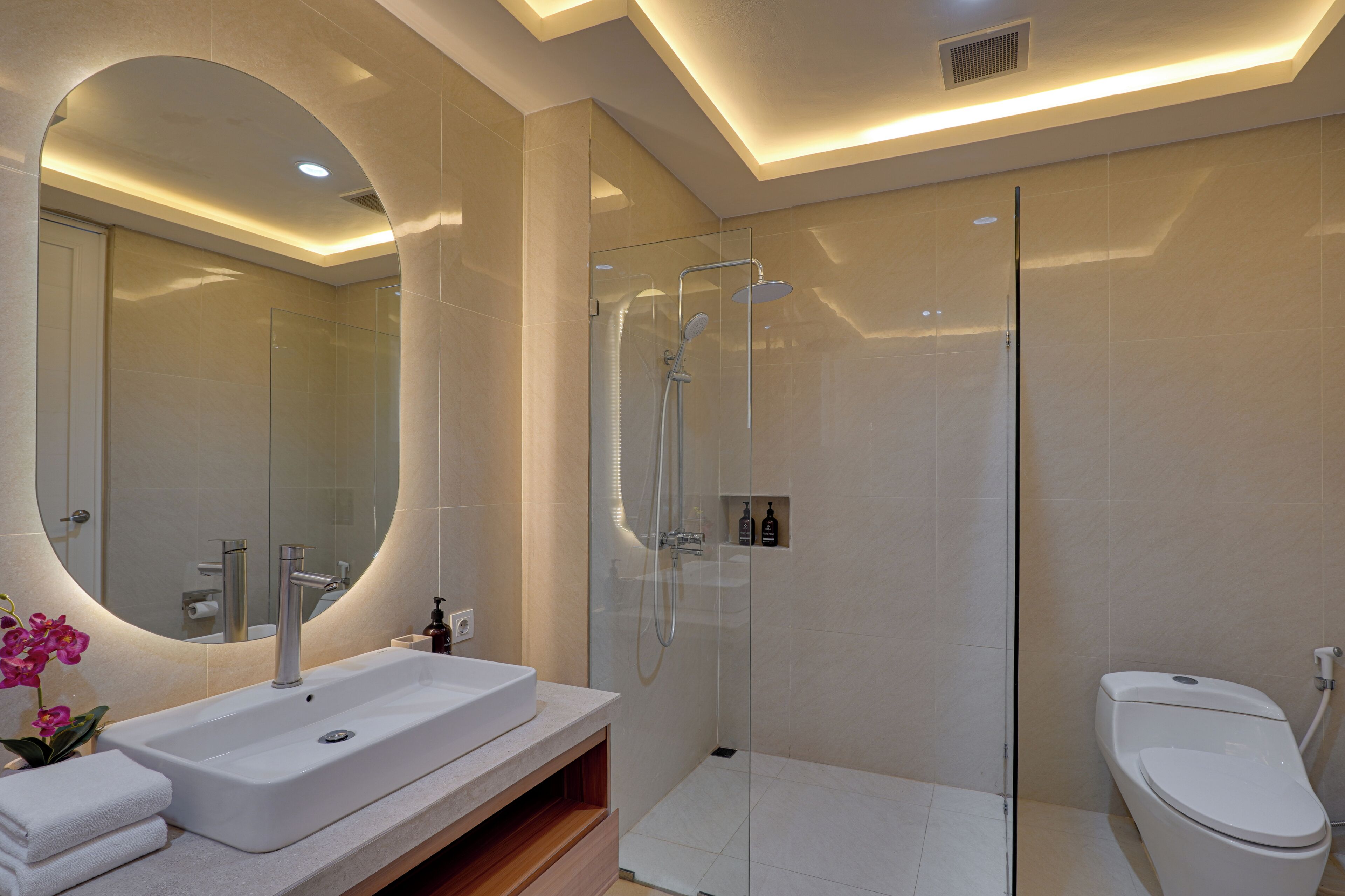 Un baño moderno con ducha de vidrio, un espejo grande y un lavamanos blanco.