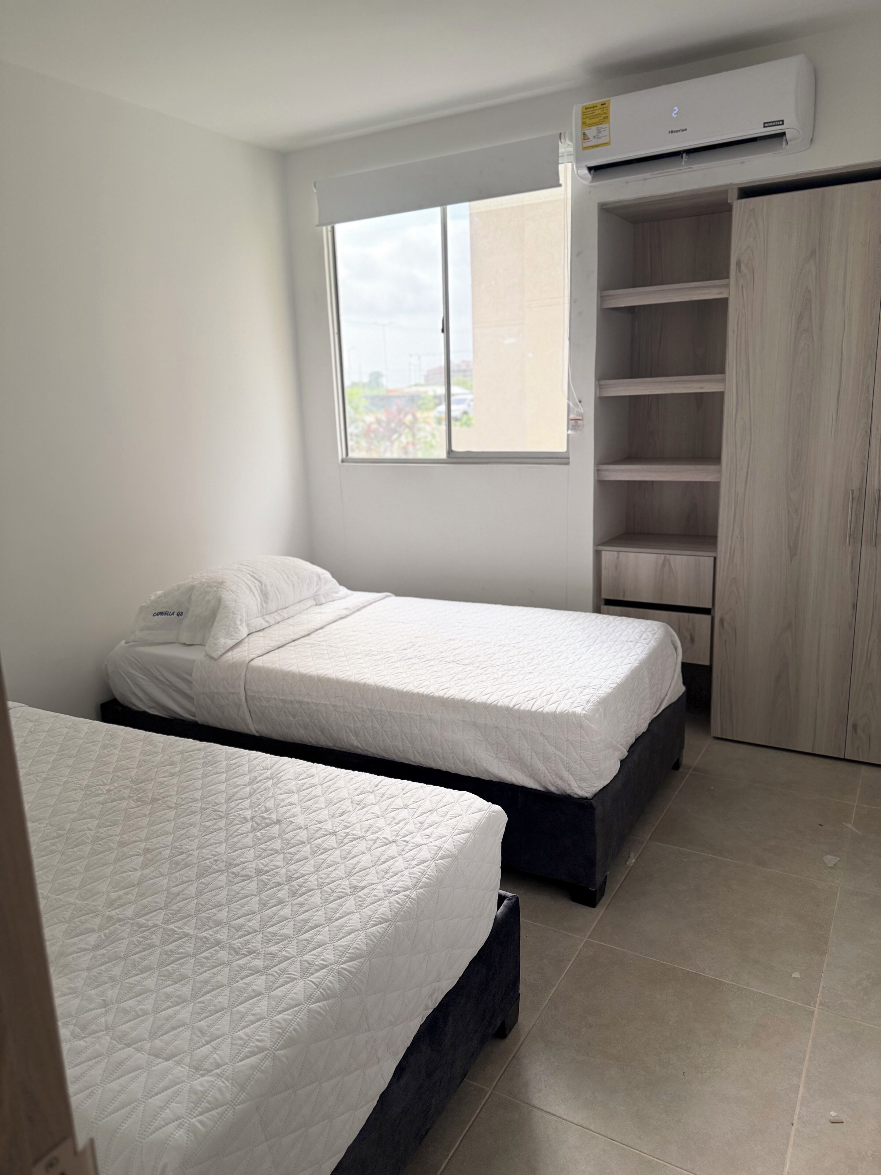 Une chambre avec deux lits, une fenêtre, un climatiseur et une armoire.