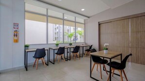 Een moderne kantoorruimte met meerdere bureaus en stoelen, grote ramen en een brandblusser aan de muur.