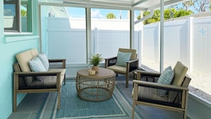 A covered patio with wicker furniture, a central round table, and a view of a white fence and greenery.