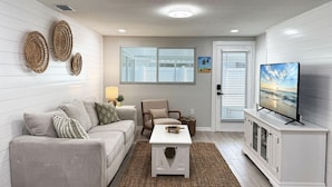 A living room with a sofa, armchair, coffee table, TV, and decorative wall art.