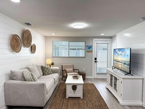A living room with a sofa, armchair, coffee table, TV, and decorative wall art.