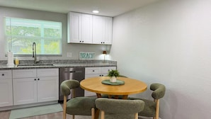A kitchen with white cabinets, a granite countertop, a sink, and a dining table with four chairs.