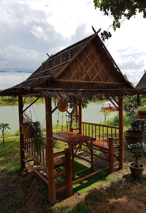 A wooden gazebo with a thatched roof overlooking a body of water. - Changthai Comfort Guest House (Udon Thani)