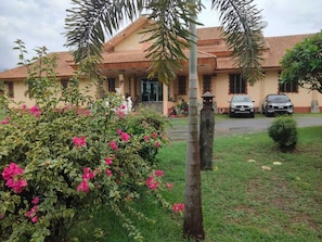 A house with a tiled roof, a garden with pink flowers, and two parked cars. - Changthai Comfort Guest House (Udon Thani)