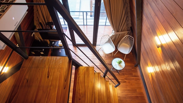 Una escalera de madera que lleva a un balcón con dos sillas blancas y una mesita.