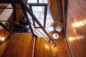 Una escalera de madera que lleva a un balcón con dos sillas blancas y una mesita.