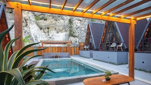 Un área de piscina exterior moderna con un deck de madera, un espacio de descanso con sillas y una planta en maceta.