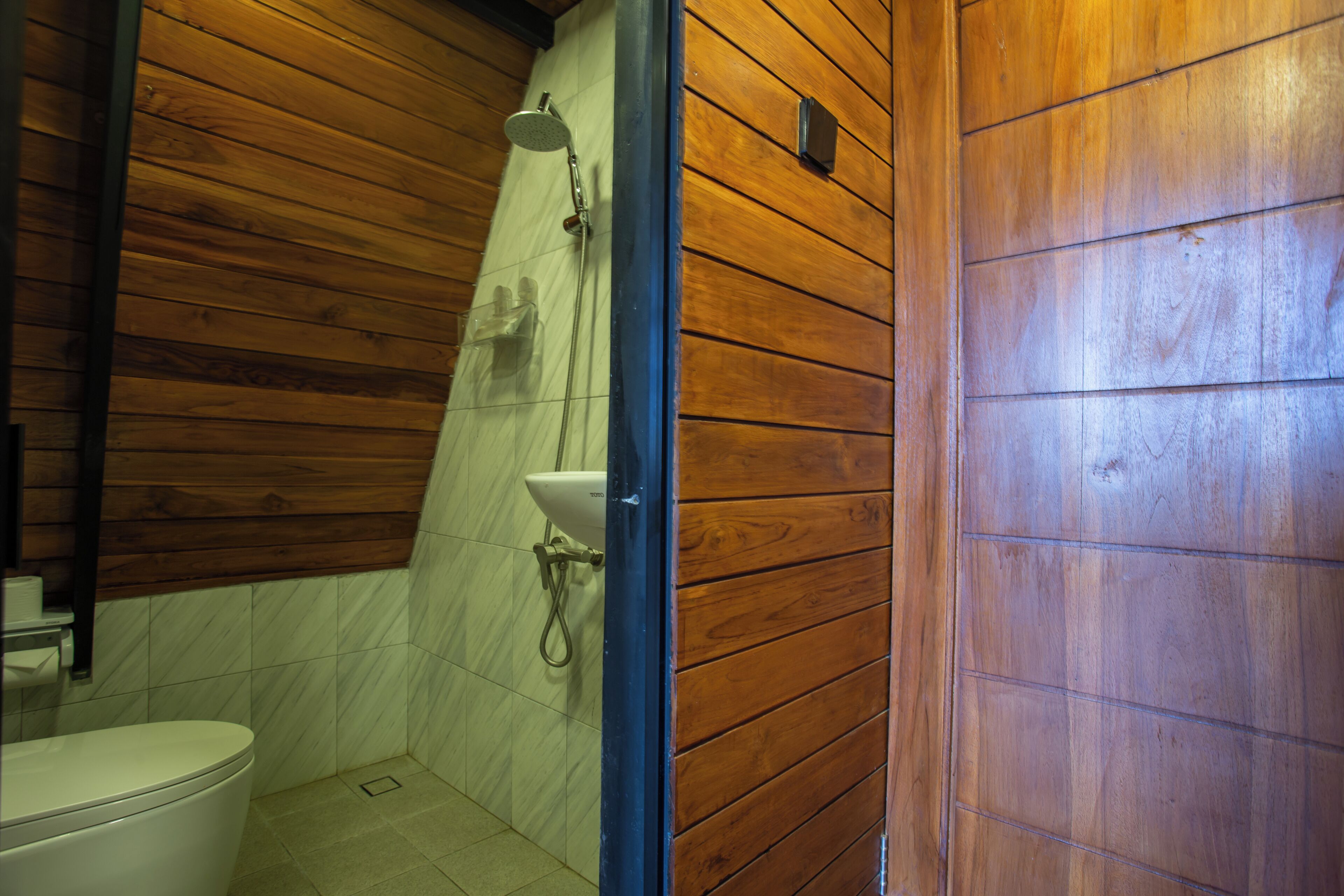 A wooden-paneled bathroom with a shower, toilet, and sink.
