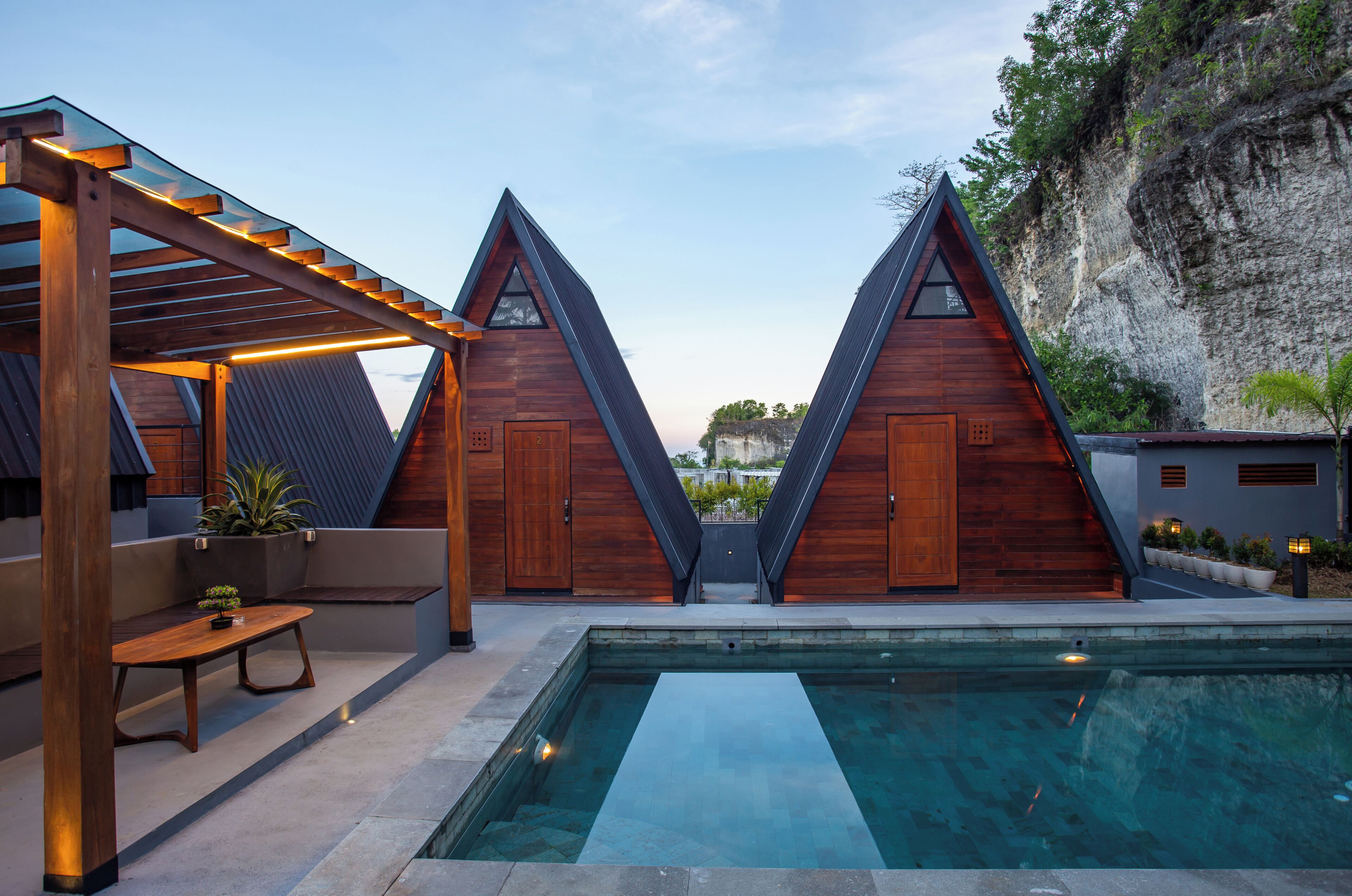 A modern building with triangular roofs, a pool, and a wooden deck with a bench.