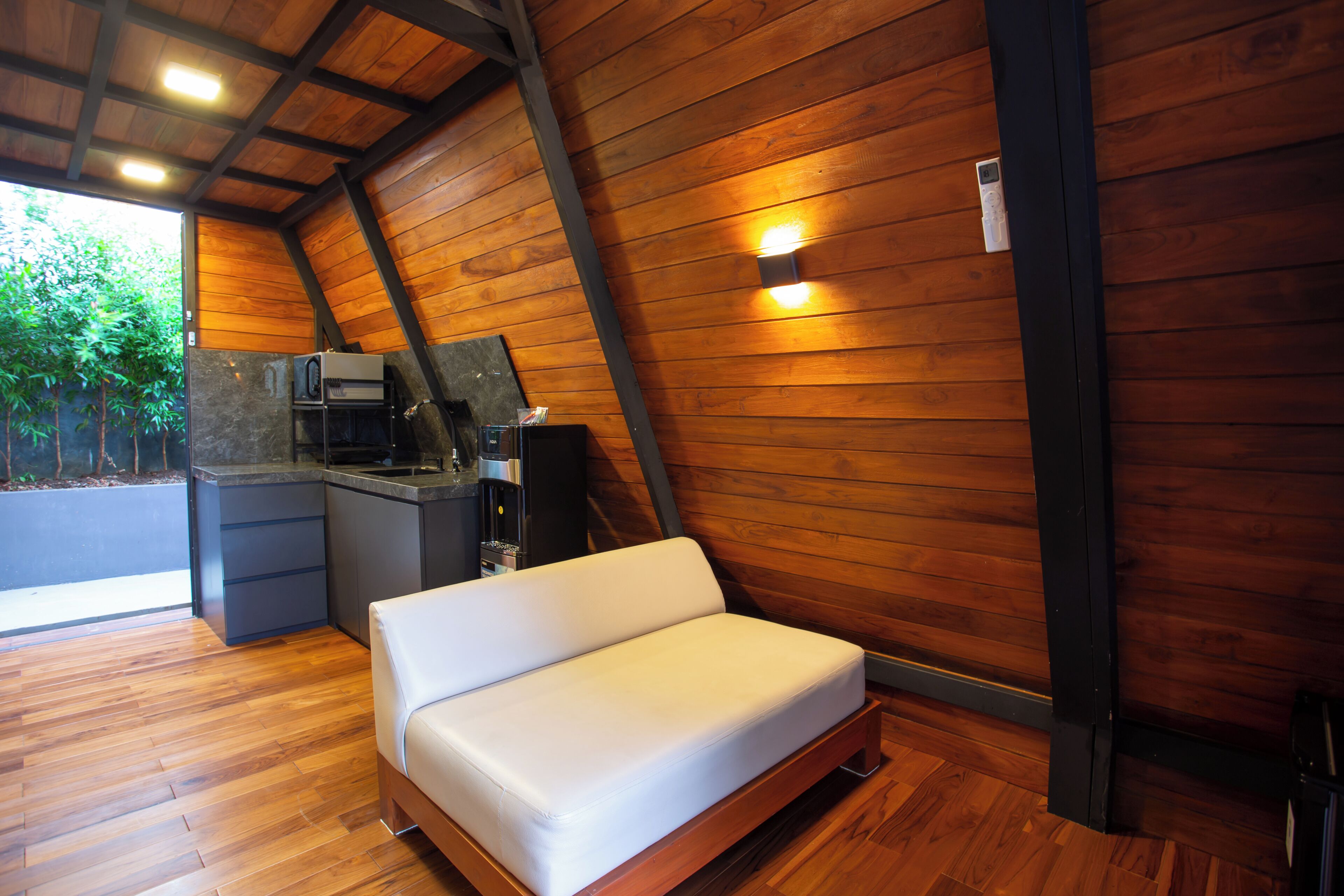 Quarto moderno estilo loft com teto inclinado de madeira, cozinha planejada e sofá branco.