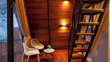 Interior de madera con una escalera, una ventana con cortinas y una pequeña mesa con una planta.