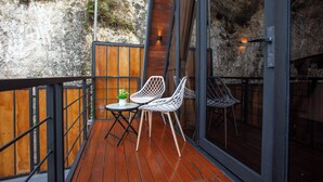 A balcony with wooden flooring, two white mesh chairs, a small round table with a potted plant, and a view of a rocky cliff. - EL Cabana (Kuta Selatan)