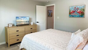 A bedroom with a bed, a dresser, a TV, and a painting of flamingos.