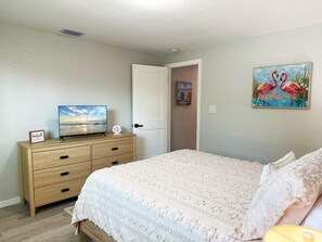 A bedroom with a bed, a dresser, a TV, and a painting of flamingos.