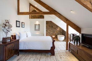 A bedroom with a wooden bed, a television, a bathtub, and a stone wall. - Landscove House - Eight Bedroom Villa, Sleeps 16 (Landscove)