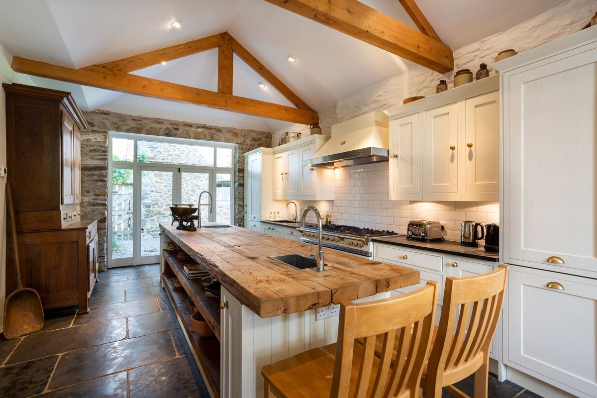 A kitchen with a wooden island, white cabinets, and a stone wall.