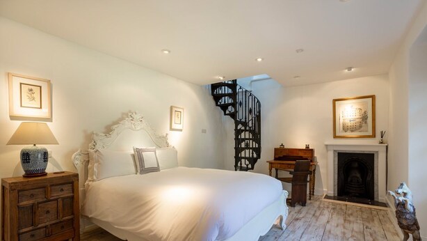 A bedroom with a large bed, a fireplace, a staircase, and a wooden floor.