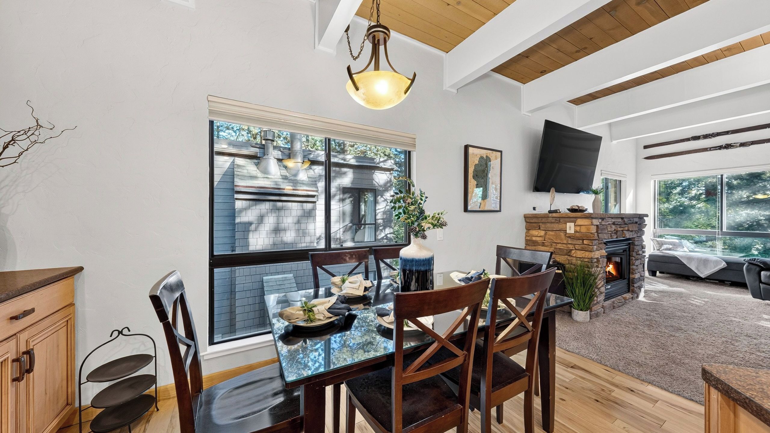 A dining area with a glass table, wooden chairs, a stone fireplace, and a TV mounted on the wall.