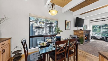 A dining area with a glass table, wooden chairs, a stone fireplace, and a TV mounted on the wall.