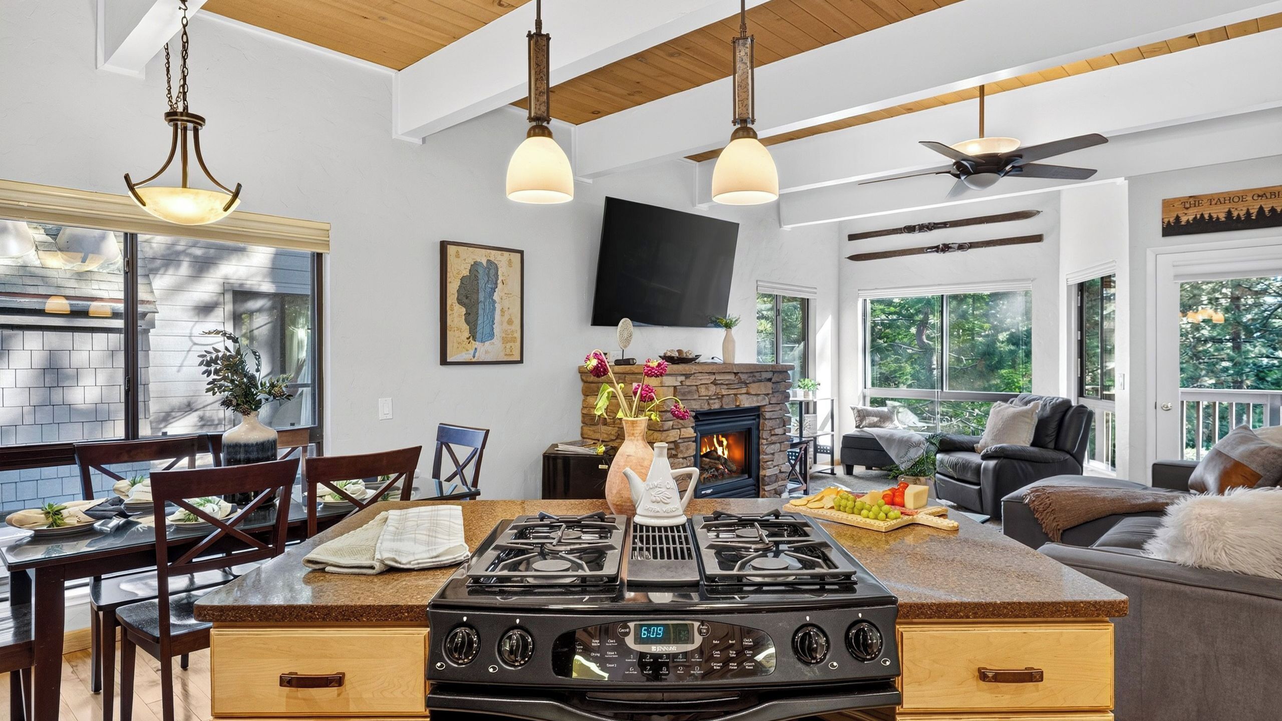 Una cocina con una isla central, un comedor con sillas, una chimenea y una sala de estar con un sofá y televisor.