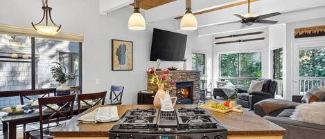 Una cocina con una isla central, un comedor con sillas, una chimenea y una sala de estar con un sofá y televisor.