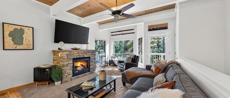 Un salon avec une cheminée en pierre, un ventilateur de plafond, un grand téléviseur et un canapé.
