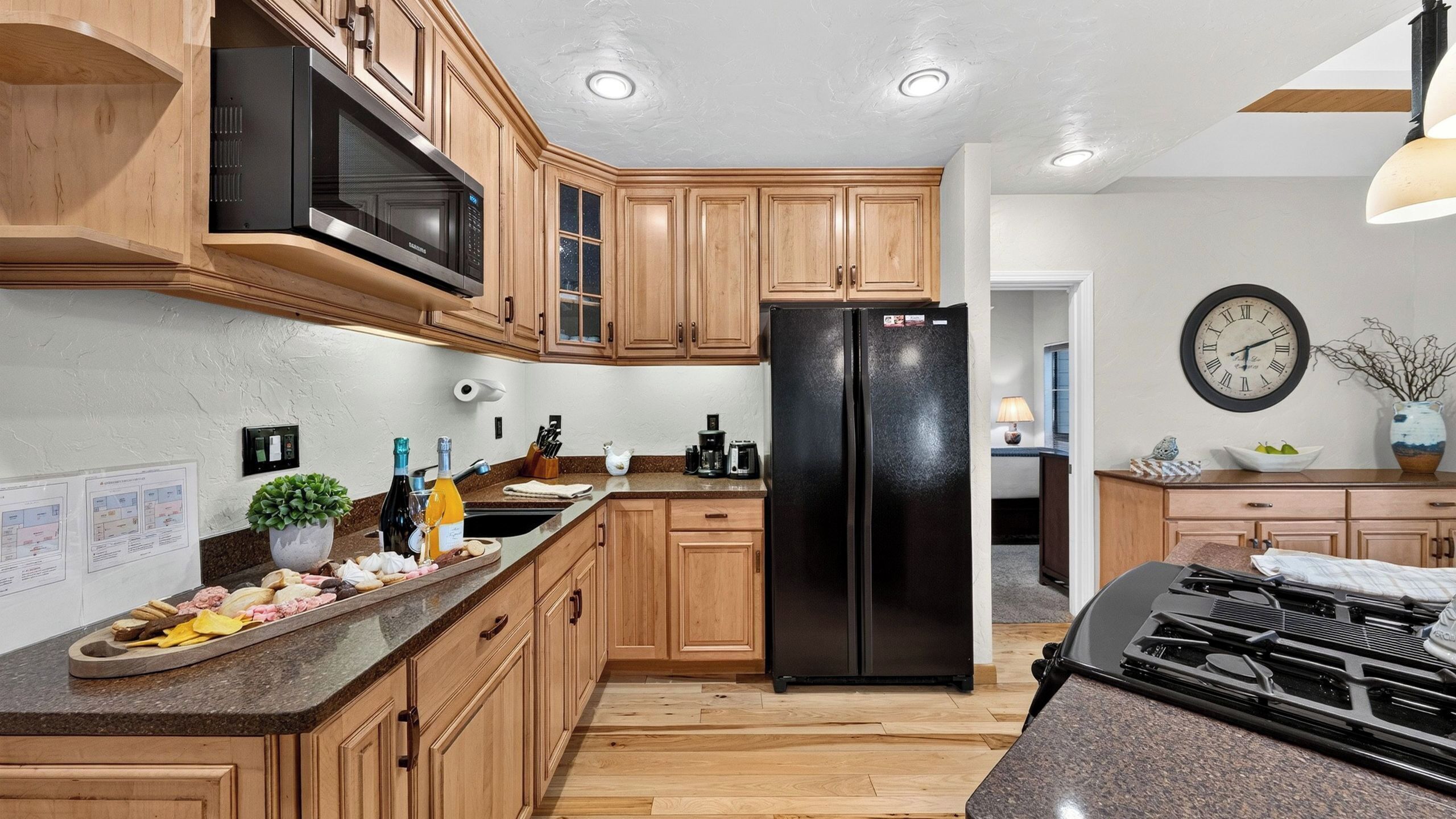 A kitchen with wooden cabinets, a black refrigerator, a microwave, a gas stove, and a clock on the wall.