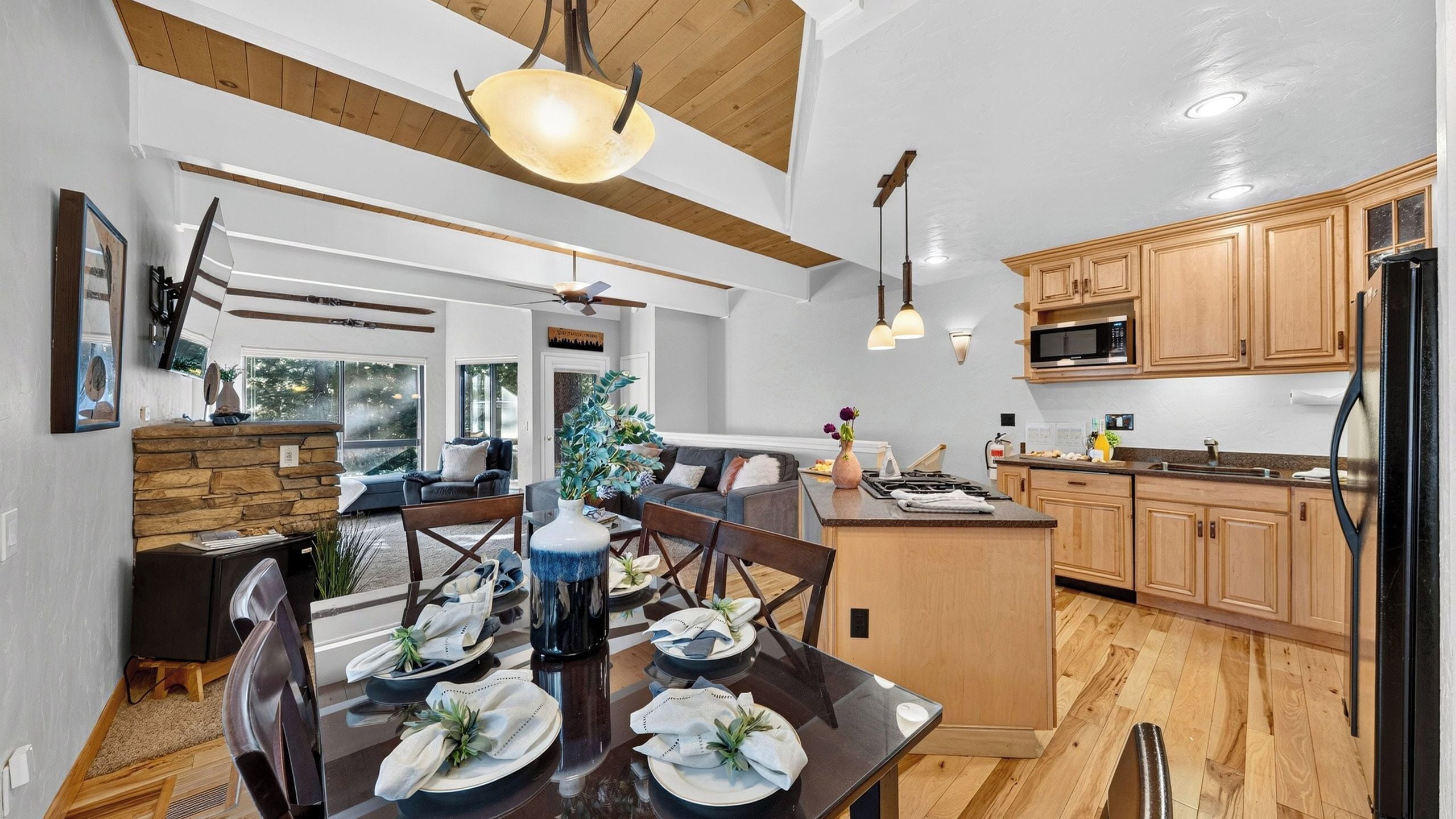 A modern kitchen with wooden cabinets, a central island, and a dining area with a glass table and chairs.