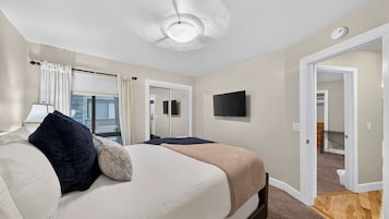 Quarto de hotel com cama, televisão, ventilador de teto e vista para o exterior.