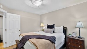 A bedroom with a bed, bedside lamps, a nightstand, a door, and a ceiling fan.