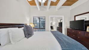 Ein Schlafzimmer mit Bett, Fernseher, Schminktisch und einem Fenster mit Jalousien.