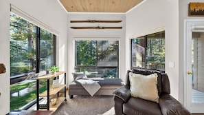 A cozy room with a large window, a comfortable couch, and a small table with a plant. - Juanita 2 by Avantstay Beamed Cabin + Pool + Balcony Diamond Peak + Lake Tahoe (Incline Village)