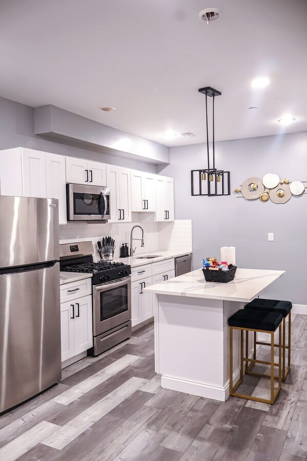 A modern kitchen with white cabinetry, stainless steel appliances, a central island, and a pendant light.